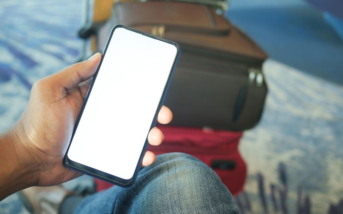 空港でスマートフォンを手にする旅行者（海外旅行の通訳アプリのイメージ）