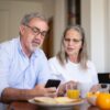 朝食のテーブルでスマートフォンの脳トレアプリを一緒に見るシニア夫婦