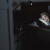 夜のベッドで画面の光に照らされながらスマホを見る女性（寝る前スマホのイメージ）