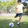 芝生のグラウンドでサッカーボールを蹴る練習をする小学生の男の子