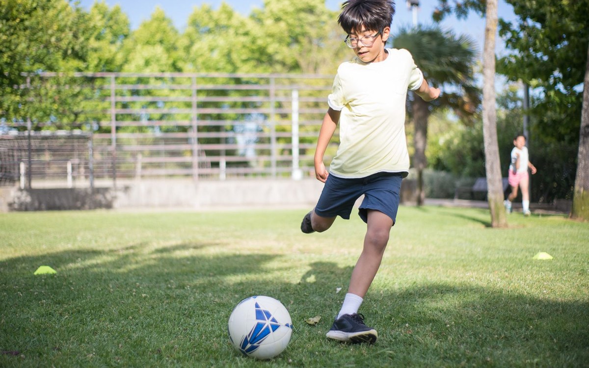 芝生のグラウンドでサッカーボールを蹴る練習をする小学生の男の子
