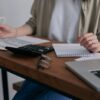 自宅の机で電卓とノートを使って家計の固定費を見直している様子